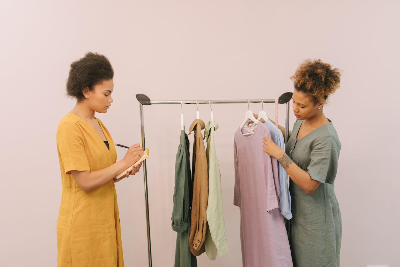 Two women working together in a fashion design setting, reviewing clothing options on a rack.